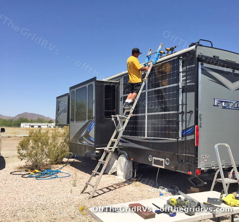 Installer on a ladder mounting solar panels on a Fuzion fifth wheel at the OffTheGridRVs shop