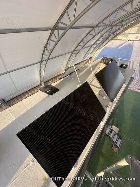Two solar panels tilted up on OffTheGridRVs manual tilt brackets on a motorhome roof under the shop canopy