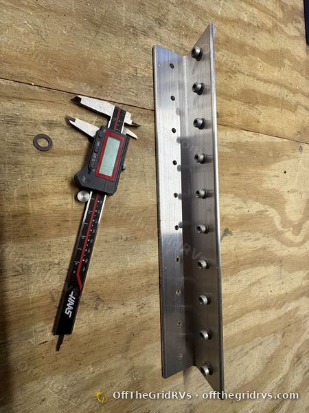 Aluminum bracket rail with threaded inserts laid next to a digital caliper on the workbench